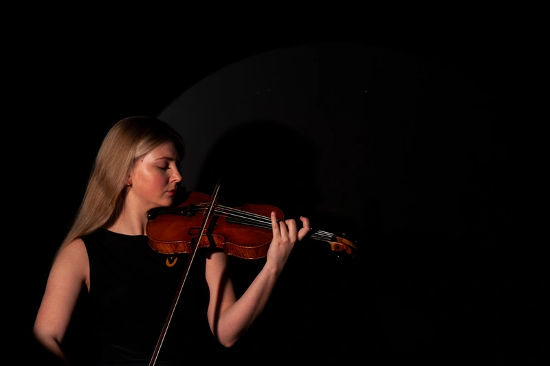 Gabrielė Santockytė playing her violin against a dark studio backdrop